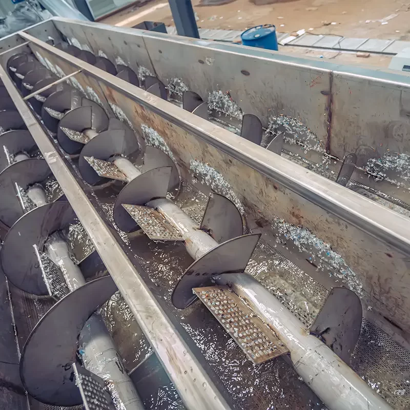 an industrial auger conveyor system, commonly used in waste management and recycling facilities. This conveyor features a series of spiral blades, or flights, enclosed in a metal trough. It is specifically designed to transport materials horizontally or at a slight incline while simultaneously mixing or breaking down the material.