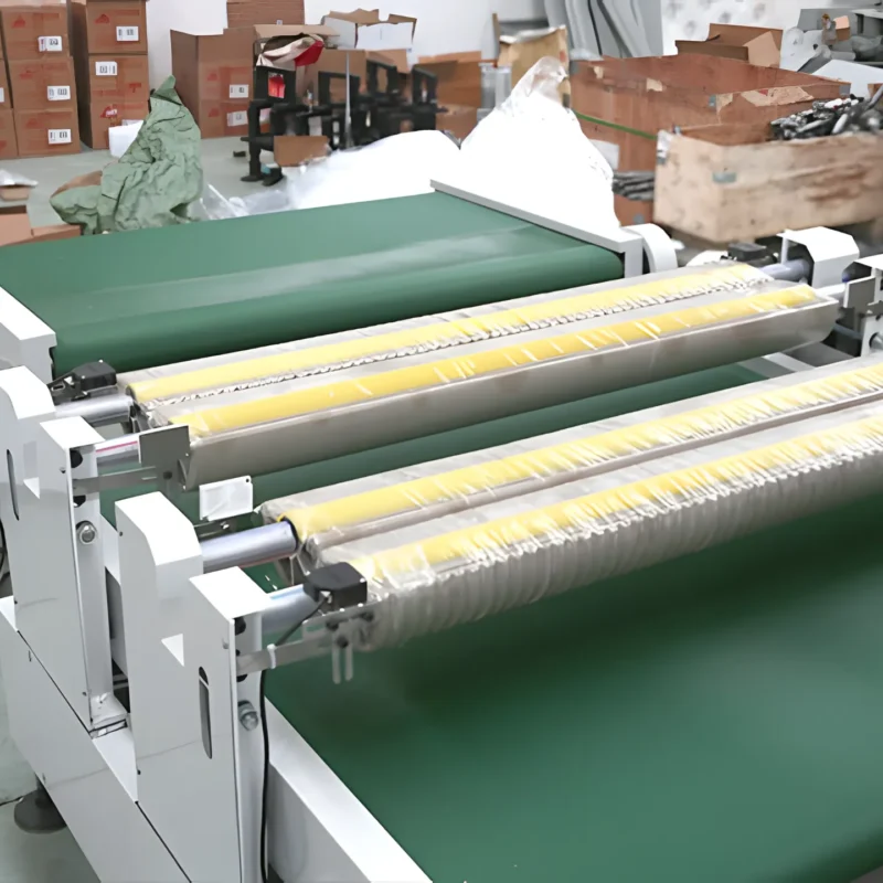 The image shows an automatic counting machine used in a PVC/nitrile glove production line. The machine features a conveyor belt system with rollers and a control panel for automated operations. The background includes boxes and other materials, indicating an industrial setting for glove manufacturing and packaging.